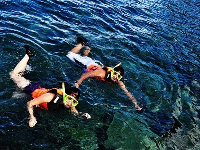 Two people snorkeling with life jackets in the clear ocean water.