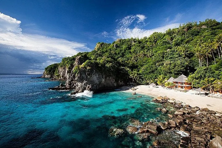 A beautiful tropical cove with clear water, sandy beach, and lush green hills.